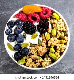 Breakfast Bowl Of Cereals Yogurt And Fruit, With Granola Oat Clusters, Blueberries, Blackberries, Apricot, Pistachio Nuts, Raspberries Oat Clusters In A Bowl, On A Black Slate Kitchen Tile