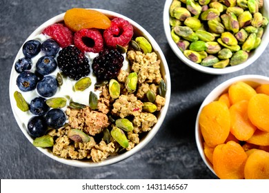 Breakfast Bowl Of Cereals Yogurt And Fruit, With Granola Oat Clusters, Blueberries, Blackberries, Apricot, Pistachio Nuts, Raspberries Oat Clusters In A Bowl, On A Black Slate Kitchen Tile