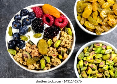 Breakfast Bowl Of Cereals Yogurt And Fruit, With Granola Oat Clusters, Blueberries, Blackberries, Apricot, Pistachio Nuts, Raspberries Oat Clusters In A Bowl, On A Black Slate Kitchen Tile