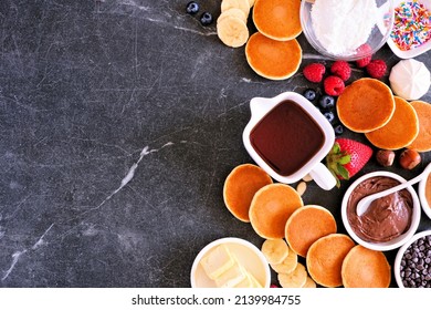 Breakfast Or Brunch Pancake Buffet Side Border. Overhead View On A Dark Stone Background. Mini Pancakes With An Assortment Of Toppings.