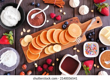 Breakfast Or Brunch Pancake Buffet Table Scene. Mini Pancakes With A Selection Of Toppings. Overhead View Over A Dark Wood Background.