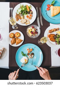 Breakfast or brunch with sparkling wine in a fancy hotel or restaurant. Female hand cutting a beautiful Poached egg, crepes with caviar on a background, mini pies and cheeses on a plate.
