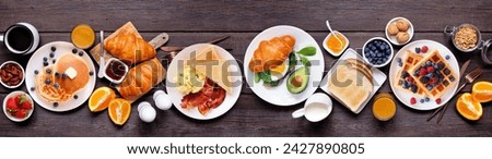 Breakfast or brunch table scene on a dark wood banner background. Top view. Assortment of sweet and savory food items.