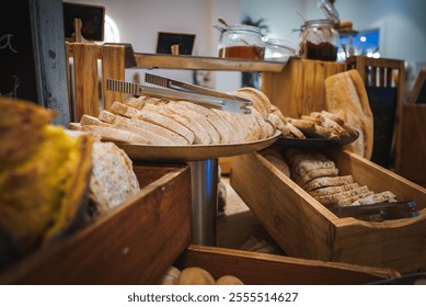 A breakfast buffet features an array of freshly baked bread in wooden trays and a metal stand, with jars of preserves in the background, in a Marrakech style setting.