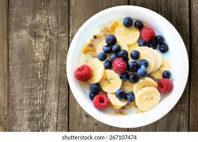 Breakfast Cereal With Blueberries, Bananas And Raspberries On A Rustic Wood Background, Overhead View   