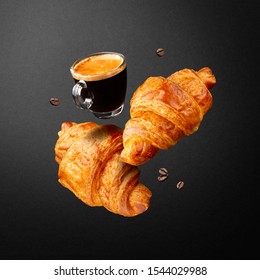 Breakfast or coffee house concept. Espresso in glass cup, croissants and beans coffee flying or falling in air on black background. - Powered by Shutterstock