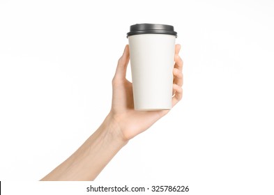 Breakfast And Coffee Theme: Man's Hand Holding White Empty Paper Coffee Cup With A Brown Plastic Cap Isolated On A White Background In The Studio, Advertising Coffee 