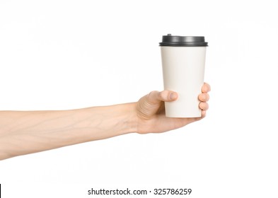 Breakfast And Coffee Theme: Man's Hand Holding White Empty Paper Coffee Cup With A Brown Plastic Cap Isolated On A White Background In The Studio, Advertising Coffee 