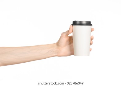 Breakfast And Coffee Theme: Man's Hand Holding White Empty Paper Coffee Cup With A Brown Plastic Cap Isolated On A White Background In The Studio, Advertising Coffee 