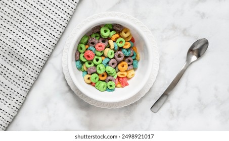 Breakfast: colorful cereal in a white bowl and plate on a white marble backdrop with a table napkin and spoon on the side.   - Powered by Shutterstock