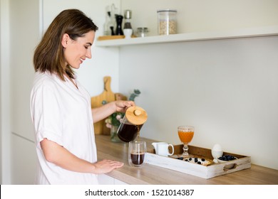 breakfast concept - woman in pajamas pouring coffee from french press in modern kitchen - Powered by Shutterstock