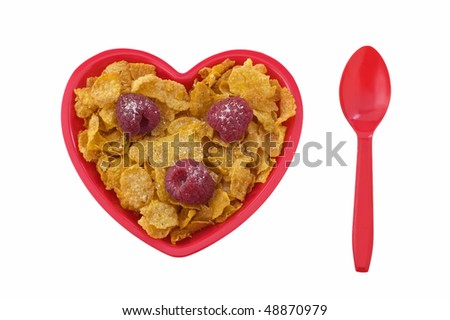 Breakfast corn flakes with raspberries in red heart dish isolated on white background