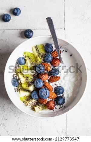 Breakfast cottage cheese with berries, kiwi, nuts and chia seeds in a white bowl, top view.
