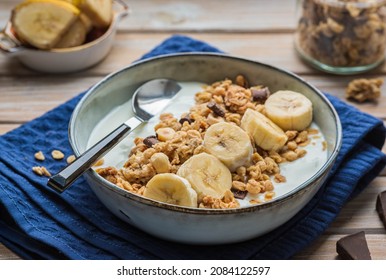 Breakfast or dessert, unsweetened yogurt with granola, dark chocolate, hazelnuts and sliced banana in a ceramic bowl on a wooden background. Breakfast recipes. Healthy food - Powered by Shutterstock