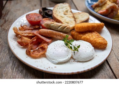 Breakfast Dish. Poached Egg On Topped By Rosemary Serve With Bacon, Sausage, Fish Chips, Tomato Grilled, Mushroom Grilled And Bread. American Breakfast.