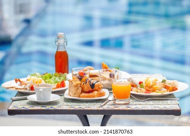 Breakfast At European Style Hotel Near Swimming Pool. Close Up Of Table With Delicious Food By The Beautiful Blue Pool Travel In Resort On Sunny Summer Day. Rest And Vacation In Luxury Hotel