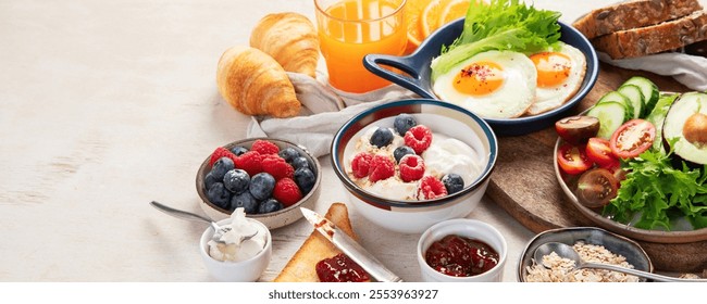 Breakfast food table. Huge healthy breakfast spread on a table with orange juice, fruit, vegetable, muesli, salmon, egg and croissants on a light background. Top view. Panorama with copy space.