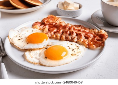 Breakfast with fried eggs and bacon close up. Fried sunny side eggs with bacon on plate, healthy keto meal.