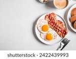 Breakfast with fried eggs, bacon, pancakes and coffee, top view, banner. Fried sunny side eggs with bacon on plate and morning cappuccino coffee. American breakfast.