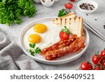 Breakfast with fried eggs, bacon and toasts on a white plate with cup of coffee on a stone background. Top view, selective focus