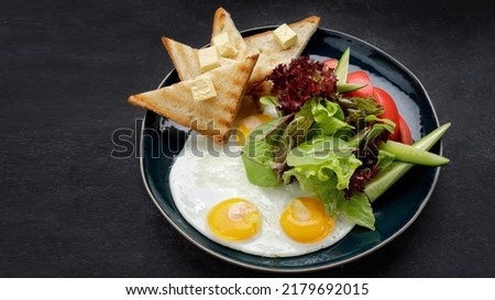 Breakfast. Fried eggs with toast with butter and vegetables, cucumbers and tomatoes. On a dark plate, against a dark background