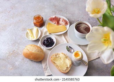 Breakfast With Hearty And Sweet Ingredients, Rolls, Egg, Coffee And Flowers On A Light Stone Background, Copy Space, View From Above, Selected Focus, Narrow Depth Of Field