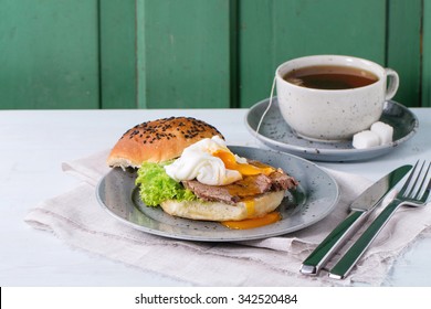 Breakfast With Homemade Sandwich With Baked Meat And Soft-boiled Egg And Cup Of Hot Pocket Tea Over White Wooden Table With Turquoise Wall At Background. 