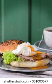 Breakfast With Homemade Sandwich With Baked Meat And Soft-boiled Egg And Cup Of Hot Pocket Tea Over White Wooden Table With Turquoise Wall At Background. 