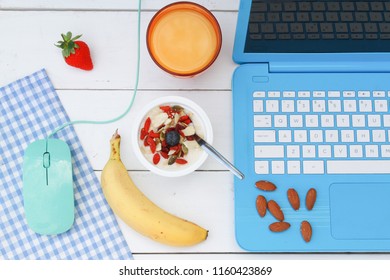 Breakfast at the laptop, including laptop, mouse, yogurt and seeds bowl, fruit and an orange juice - Powered by Shutterstock