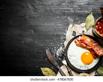 Breakfast In The Morning. Beans With Fried Egg And Bacon. On A Black Wooden Background.