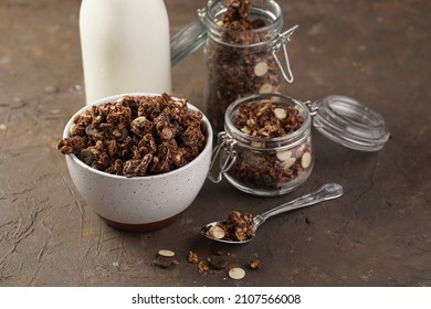 Breakfast muesli cereal with chocolate chips and nuts in several jars and bowl, bottle of milk, brown wooden surface - Powered by Shutterstock