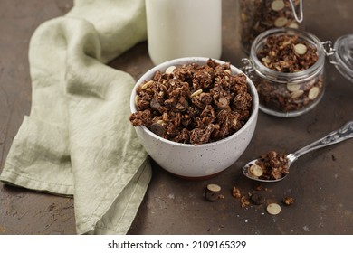 Breakfast muesli cereal with chocolate chips and nuts in several jars and bowl, bottle of milk, brown wooden surface - Powered by Shutterstock