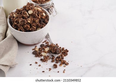 Breakfast muesli cereal with chocolate chips and nuts in several jars and bowl, bottle of milk, white surface - Powered by Shutterstock