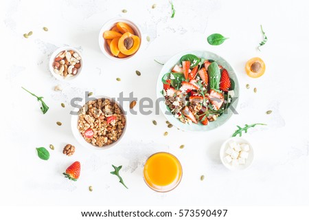 Breakfast with muesli, strawberry salad, fresh fruit, orange juice, nuts on white background. Healthy food concept. Flat lay, top view