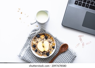 Breakfast In The Office With A Bowl Of Cereal, Fruit And Milk On A White Desk With A Laptop. Top View, Modern. 