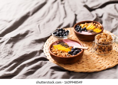 Breakfast On Bed With Smoothie Bowl With Granola, Mango, Yogurt And Blueberry On Grey Background