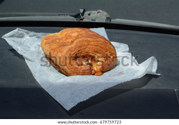 Breakfast on the go of bakery ham and Swiss\
cheese croissant on automobile\
dashboard
