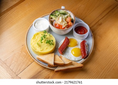 breakfast on a plate: sausages, fried eggs, mashed potatoes, vegetables, salad, bread and sauce - Powered by Shutterstock