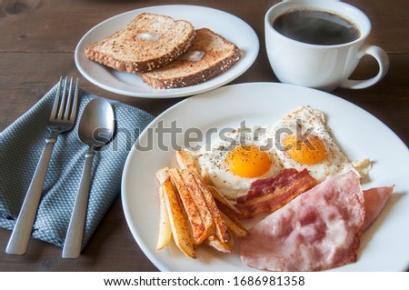 Breakfast on a table with eggs ham bacon fries and toast with butter on top of toast, and black coffee