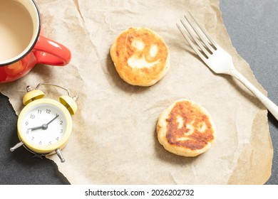 Breakfast on the table, good morning concept, top view: cup of coffee, two cheese cakes with angry painted faces, fork, alarm clock on baking paper. Funny early morning, Halloween, funny food theme.