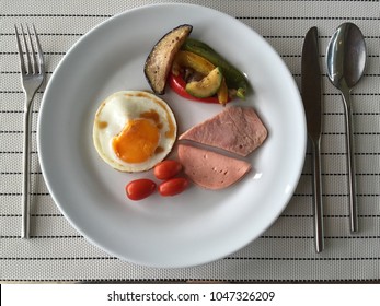 Breakfast On A White Plate With Fried Egg, Toast Ham, Cherry Tomato,zucchini, Bell Pepper On Black And White Stripe Place Mat With Fork Spoon And Butter Knife Aside