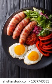 Breakfast Pigs In Blankets Fried Sausages Wrapped In Bacon, Eggs, Sauce And Fresh Salad Close-up On A Plate. Vertical Top View From Above
