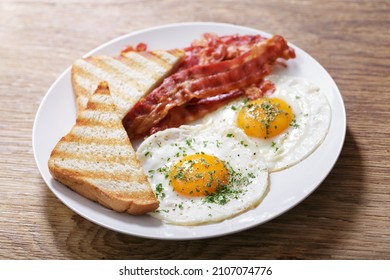 breakfast with plate of fried eggs, bacon and toast on a wooden table - Powered by Shutterstock
