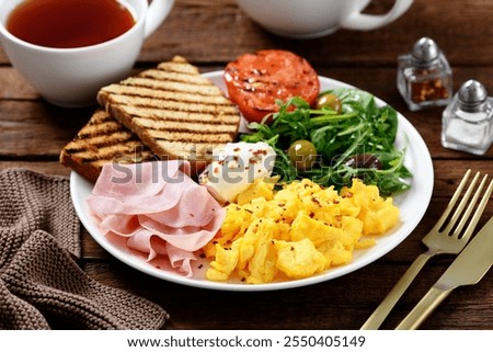 Breakfast plate with scrambled egg, ham, fresh salad and toasted bread. Wooden background    