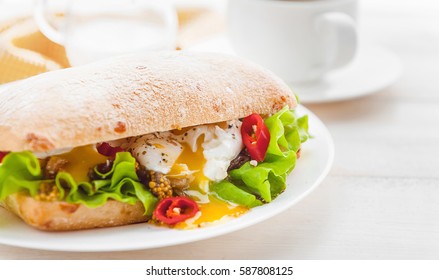 breakfast in a rustic style on a white wooden surface. ciabatta with poached egg and grain mustard with a hot cup of coffee and fresh