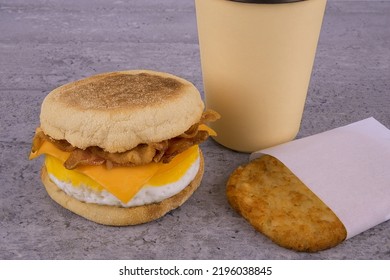 Breakfast sandwich with coffee and hash brown on concrete table. English muffin, egg, cheese and sausage. - Shutterstock ID 2196038845
