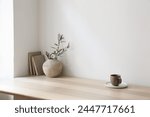 Breakfast, scandi indoor interior still life. Minimal home design concept. Beige ceramic vase with olive tree branches. Cup of coffee, tea on wooden table, desk with old books. Empty beige wall mockup