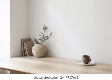 Breakfast, scandi indoor interior still life. Minimal home design concept. Beige ceramic vase with olive tree branches. Cup of coffee, tea on wooden table, desk with old books. Empty beige wall mockup - Powered by Shutterstock