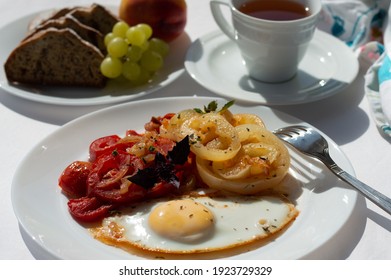 Breakfast of scrambled eggs and vegetables, in the background a cup of tea, a banana muffin and grapes with peaches on a plate.