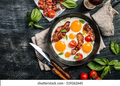 Breakfast Set. Pan Of Fried Eggs With Bacon And Fresh Tomato On Black Background, Top View